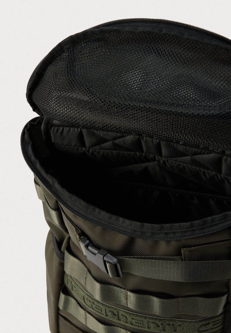 Zaino verde in nylon di forma cilindrica, con apertura con cerniera e parte superiore in rete, più dettagli in tessuto tecnico per punti di aggancio.