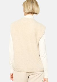Beez värvusega ilma varrukateta kampsunivest, mis on valmistatud pehmest ja tekstuuriga kangast, ribidega alläärega, laia lõikega ja minimalistliku disainiga.