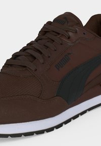 Καφέ αθλητικό παπούτσι Puma με μαύρο λογότυπο και ρίγες, σχέδιο με κορδόνια, λευκή ενδιάμεση σόλα και υφή στο μπροστινό μέρος για κράτημα και ανθεκτικότητα.