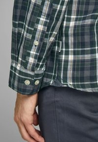 Groen- en marineblauw geruit overhemd met knopen, met witte en gele accenten, voorzien van een ronde manchetknoop en een label zichtbaar nabij de zoom.