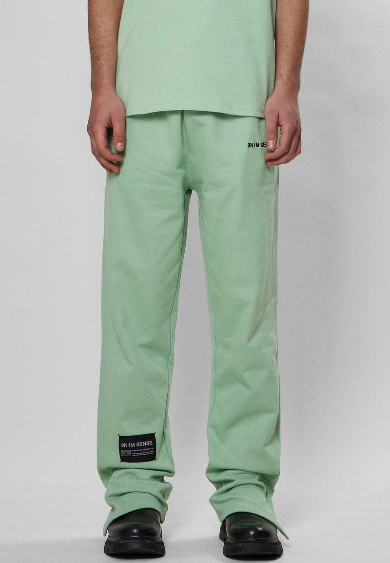 Helle grüne Sweatpants aus weichem Stoff, mit einem elastischen Bund, Seitentaschen und einem schwarzen Etikett am Saum mit weißem Text.