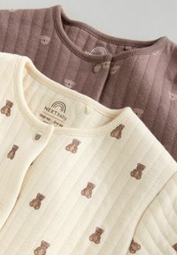 To babycardigans, en i creme med bamseprint og den anden i brun med lodrette striber og bamsemotiver. Blødt bomuldsstof, knaplukning.