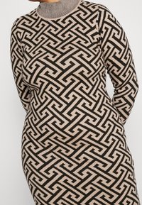 Robe tricotée avec un col haut, présentant un motif géométrique noir et beige, ajustée et à manches longues. Tissu texturé.