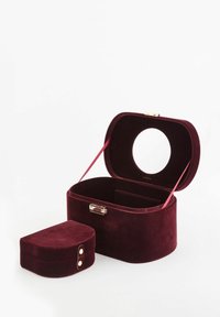 Aksamitne, bordowe etui do przechowywania o zaokrąglonym kształcie, z złotymi elementami i otwierane od góry. Zawiera mniejszy, dopasowany owalny pokrowiec z zapięciem na guzik.