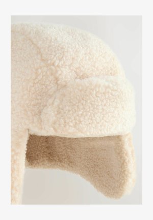 Krémová čepice z umělé kožešiny s ušima, která má měkký, texturovaný povrch a zaoblený tvar pro tepelnou izolaci a pokrytí.