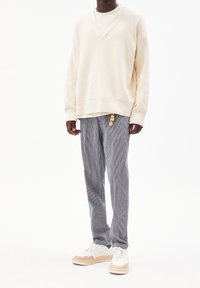 Felpa oversize color crema con scollatura a V, abbinata a pantaloni a righe e Sneakers bianche con accenti marroni.