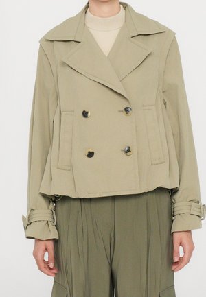 Beige double-breasted cropped jacket with wide lapels and buttoned cuffs worn over a light turtleneck and paired with olive pleated pants.