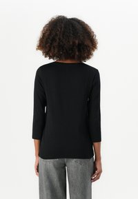 Black three-quarter sleeve top made of smooth fabric, with a rounded neckline and relaxed fit, paired with gray wide-leg pants.