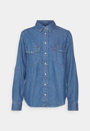 Camicia in denim blu con bottini, maniche lunghe, due tasche sul petto e colletto. Presenta un logo Levi's sulla tasca sinistra.