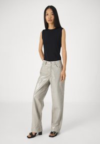 Μαύρο αμάνικο τοπ συνδυασμένο με λαμπερά ανοιχτό γκρι παντελόνια σε στιλ κροκοδείλου με φαρδιά πόδια και μαύρες σανδάλια με λεπτό τακούνι.