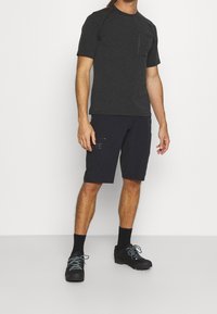 Mans atletiska outfit med en mörkgrå t-shirt med kort ärm och ficka, samt marinblå shorts med sidoglider, kombinerat med svarta skor.