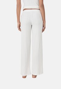 Pantalones de pierna ancha blancos y acanalados con una cinturilla alta y elástica. El dobladillo presenta un detalle deshilachado. Textura suave, diseño minimalista.