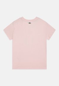 Camiseta de algodón de mangas cortas en color rosa, con un escote redondo y un pequeño logo verde en la parte posterior cerca del cuello.