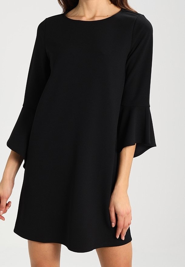 Robe noire longueur genou avec manches évasées aux trois quarts portée par une personne devant un fond clair uni.