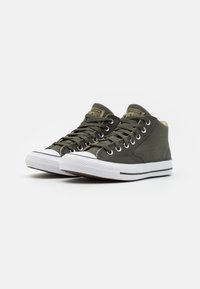 Zelené plátěné vysoké tenisky s bílými gumovými podrážkami, černými pruhy a kovovými očky. Pozoruhodné zlaté logo na jazyku.