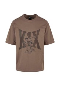 Brūns kokvilnas T-krekls ar lielu melnu grafiku, kas attēlo basketbola spēlētāju un uzrakstu "K1X". Īsas piedurknes un apaļa kakla izgriezums.