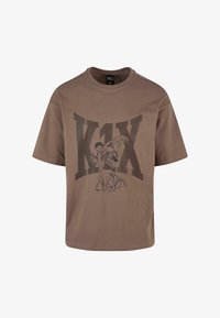 Camiseta de algodón marrón que presenta un gran estampado gráfico negro de un jugador de baloncesto y el texto "K1X". Manga corta y cuello redondo.
