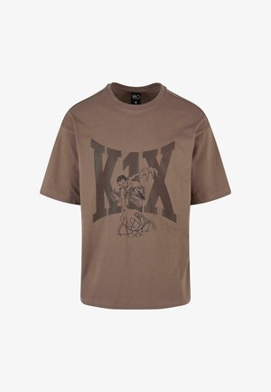 Barna pamut póló, nagy fekete grafikával egy kosárlabdázóról és a "K1X" felirattal. Rövid ujjú és kerek nyakkivágású.