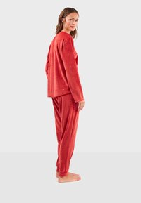 Ensemble de loungewear en velours rouge comprenant des manches longues et un pantalon, agrémenté de petits points ressemblant à de l'or. Texture douce, coupe décontractée et couleur unie.
