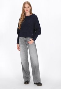 Maglione lavorato a maglia navy con motivo strutturato e ampio colletto, abbinato a jeans a zampa d'elefante grigi sbiaditi e scarpe nere.