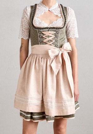 Kobieta ubrana w tradycyjną dwukolorową zielono-różową sukienkę dirndl z koronkową bluzką, różowym fartuchem związanym kokardą w talii oraz ozdobnym gorsetowym przodem.