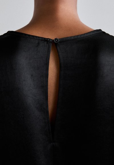 Black top featuring a round neckline and a vertical back slit. Fastened with a black button at the neck. Smooth, lightweight texture.