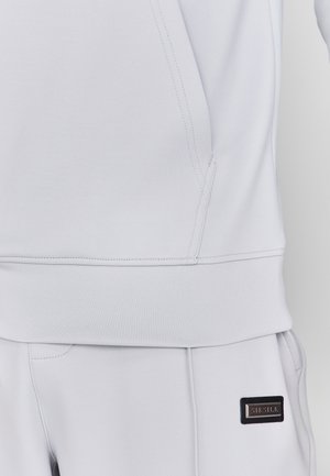 Vaaleanharmaa collegepaita, jossa on pehmeä rakenne, korkea kaulus, ribbireunat ja pieni musta merkkilappu sivulla.