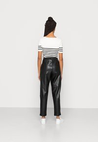 Pantalons noirs en simili cuir taille haute avec une coupe décontractée, associés à un haut à manches courtes blanc et noir à rayures. Baskets blanches.