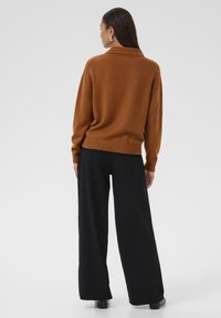 Brown knit sweater with a high collar and ribbed hem, paired with black wide-leg pants and ankle boots. Smooth texture, modern fit.