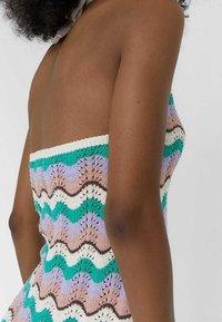 Sukienka dzianinowa z bezrękawowym krojem, w wielokolorowy falisty wzór w zieleni, lawendzie, brązie, kremie i bieli. Teksturowana tkanina.