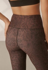 Hoch taillierte Leggings mit einem strukturierten braunen Muster und dunklen Akzenten, ausgestattet mit einem glatten Bund und Nahtdetails entlang der Nähte.
