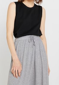 Haut sans manches noir associé à une jupe rayée grise et blanche avec une taille à cordon de serrage et une coupe ample et fluide.