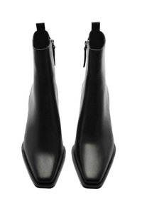 Bottines en cuir noir avec bout pointu, texture lisse, œillet de traction à l'arrière et détail de fermeture éclair latérale. Talon robuste et silhouette élégante.