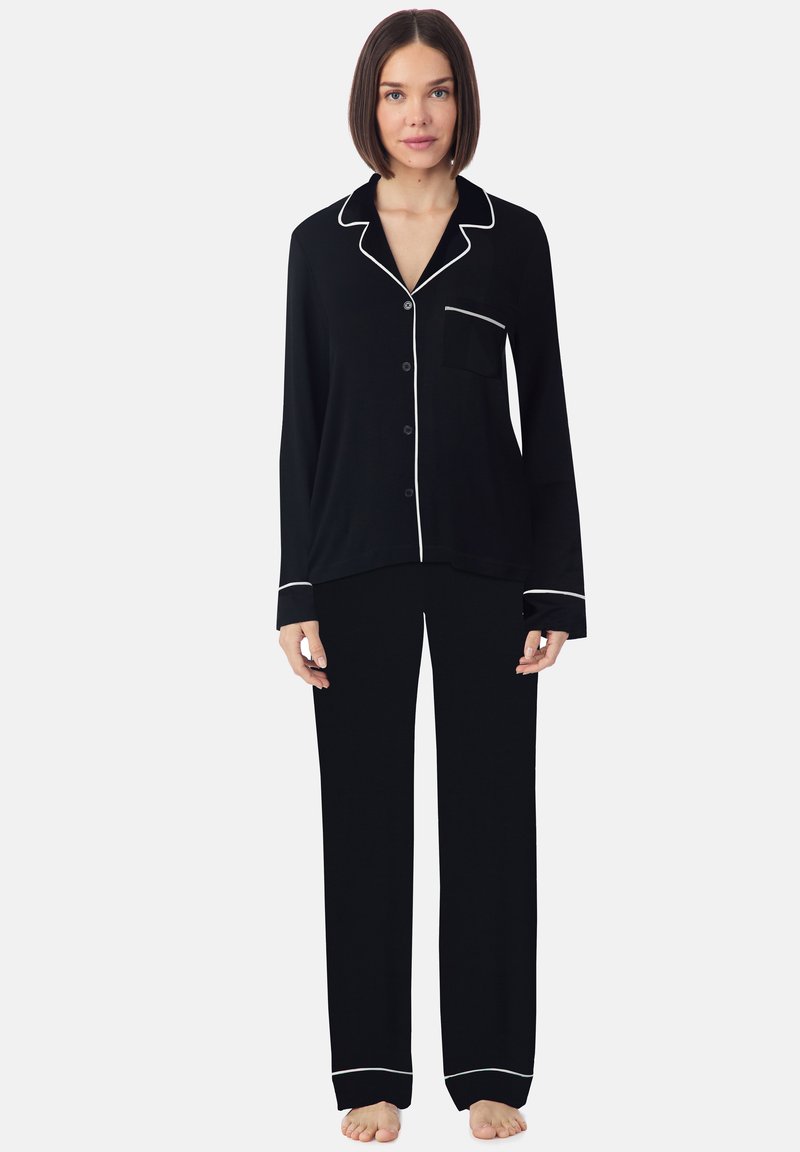 Ensemble de pyjama noir comprenant un haut à boutons avec col, poche et garnitures blanches, associé à un pantalon large assorti. Tissu doux au toucher.