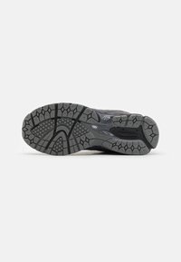 Semelle d'une chaussure de sport grise et noire avec un motif texturé pour l'adhérence et la flexibilité, présentée sur un fond uni.
