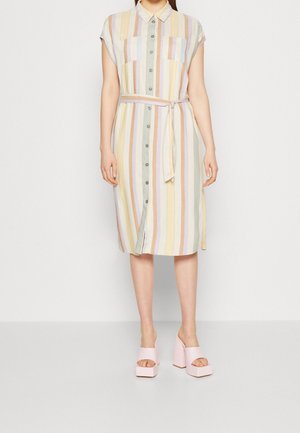 Mujer con un vestido de rayas verticales pastel hasta la rodilla, abotonado, con cinturón en la cintura y sandalias rosas de plataforma alta y punta abierta.