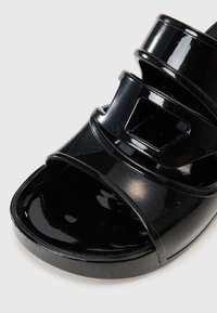 Sandale slide din piele patent neagră, cu curele late, vârf rotund și o talpă ușor ridicată. Prezintă un design cu decupaje pe curele.
