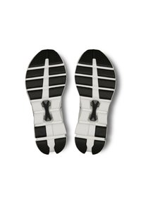Semelles de chaussures de sport en noir et blanc avec des motifs texturés, présentant une traction en caoutchouc épais et un détail de marque central. Design flexible.