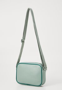 Obdélníková crossbody taška z jemné mátově zelené kůže s texturovaným povrchem, vybavená odpovídajícím popruhem a kontrastním lemem.