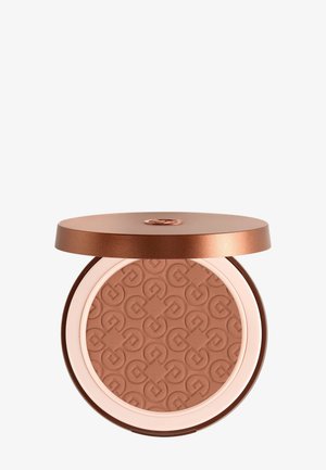 Bronzefarbener Kompaktpuder mit eingeprägtem geometrischem Muster, offener Deckel zeigt strukturierte Oberfläche und metallic-braune Verpackung.