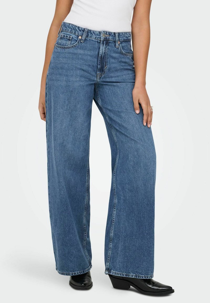 Jean en denim à jambes larges de couleur bleu clair, comprenant cinq poches, une braguette à boutons, et des détails cousus. Le tissu est doux avec une finition légèrement délavée.