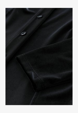 Schwarzes Samtprodukt mit Knopfverschluss, weicher Textur und sorgfältig verarbeiteten Nähten. Nahaufnahme, die die Stoffdetails hervorhebt.