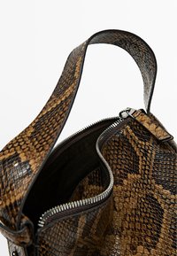 Borsa a tracolla con motivo a serpente marrone, dalla superficie texture, dotata di chiusura a zip e una robusta tracolla. L'interno è foderato in tessuto scuro.