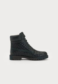 Black woven leather ankle boot with a padded collar, lace-up front, and textured rubber sole. Features a subtle green accent on the side.