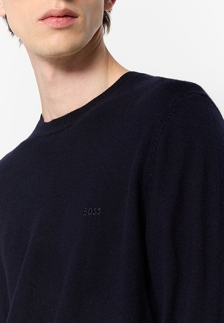 Navyblauwe gebreide trui met een ronde halslijn en geribde randen. Voorzien van een geborduurd logo op de borst, met een soepele textuur.