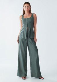 Haut sans manches vert foncé avec un décolleté droit et un devant à boutons, associé à un pantalon taille haute à jambes larges en tissu assorti.