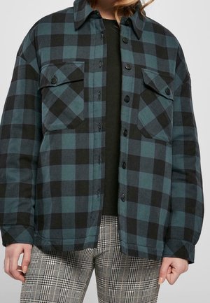 Personne portant une veste à carreaux bleu sarcelle et noir à boutons sur une chemise noire et un pantalon à carreaux gris, montrée des épaules à la mi-cuisse.
