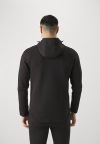Sudadera negra con capucha, de textura suave y mangas largas. Presenta cordones ajustables en la capucha y un dobladillo ligeramente curvado.