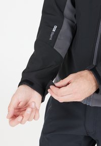 Schwarze und graue Jacke mit Reißverschluss vorne, verstellbarem Klettverschluss am Ärmel und weichem Material. Das Design auf der Rückseite enthält ein "WARM 800"-Etikett.