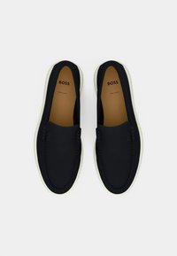 Sorte slip-on sko med en glatt overflate, hvit gummisåle og subtil stikking. Innvendig har de en beige såle med logo.